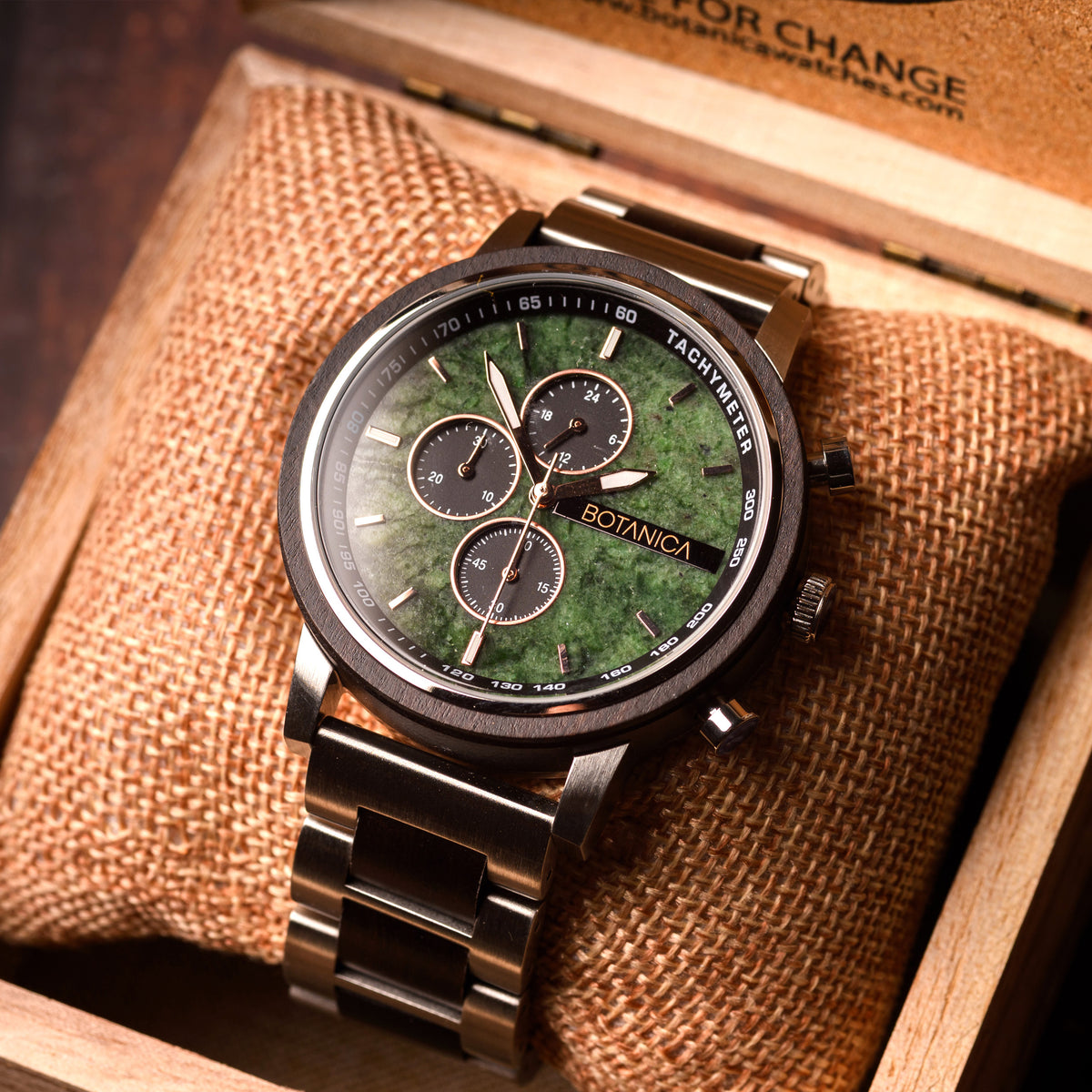 Watch with green stone face and metal band on brown textured fabric
