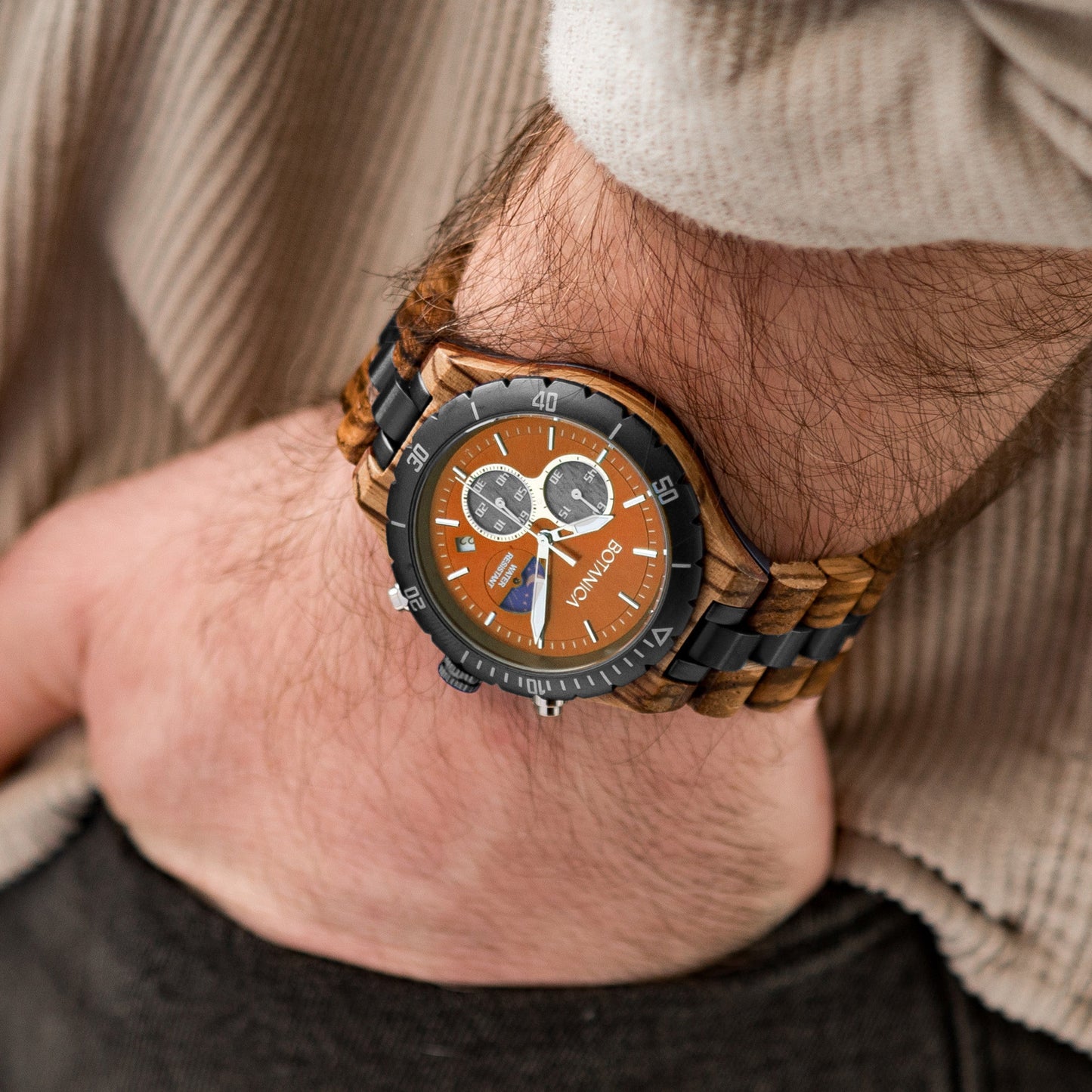 A person wearing a Zebrano wooden and metal bracelet watch with a Orange dial and rose gold accents.