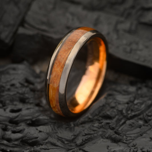 A Mens 6mm Tungsten steel ring with single groove whiskey barrel inlay and rosegold inner ring resting on Charcoal slate bed