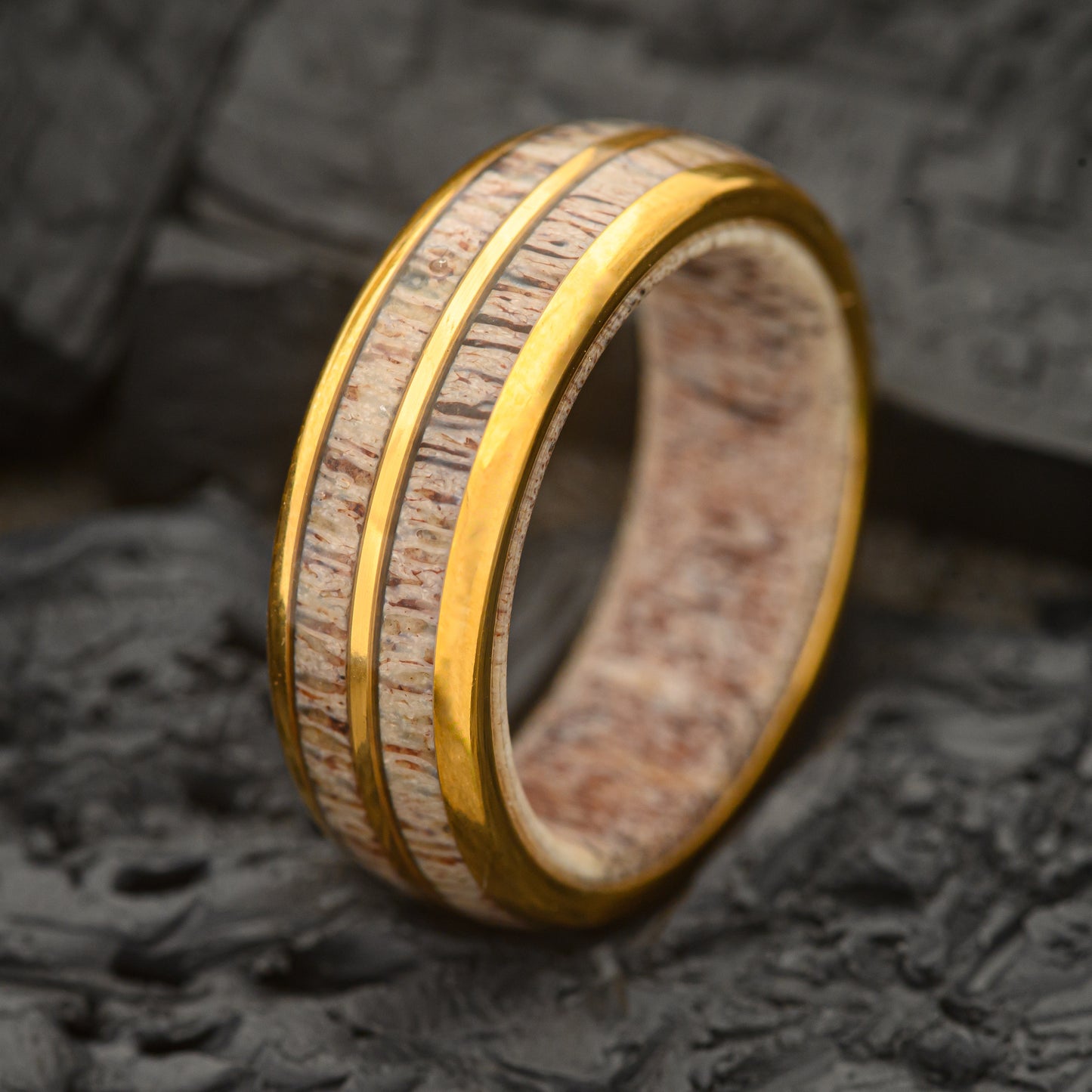 A Mens Dual Band gold and tungsten steel ring 8mm with a Deer Antler inlay and inner ring sitting on a charcoal rock