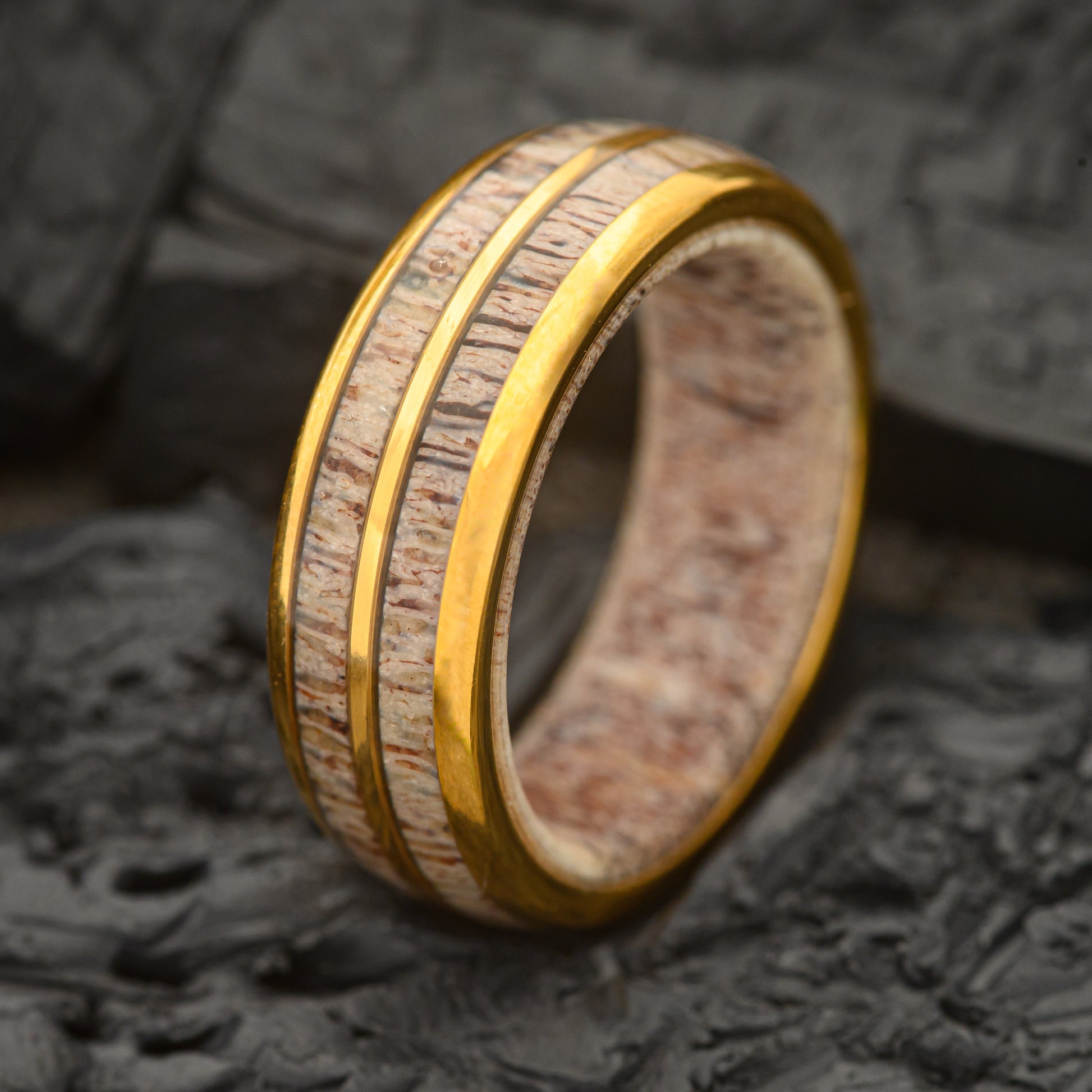 A Mens Dual Band gold and tungsten steel ring 8mm with a Deer Antler inlay and inner ring sitting on a charcoal rock