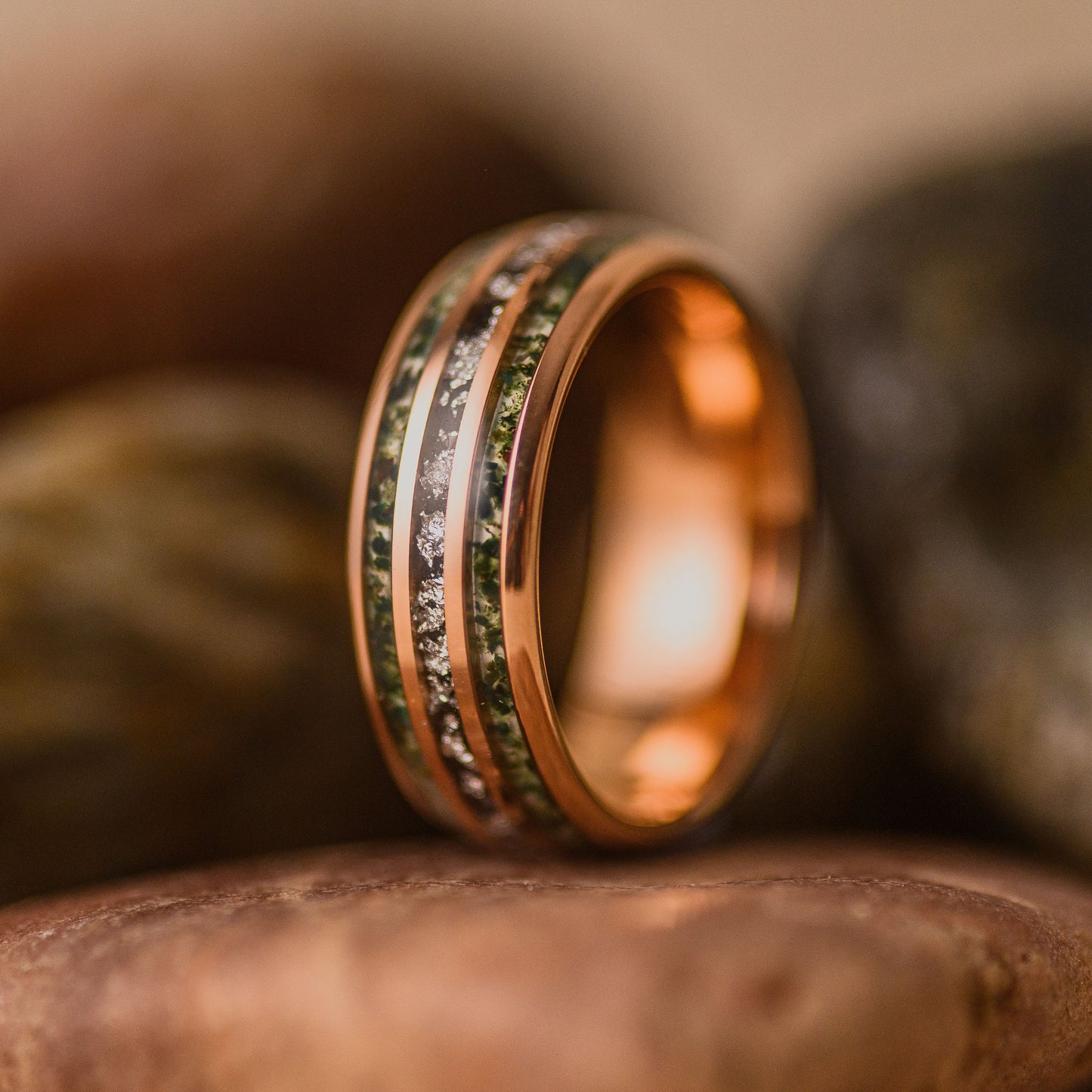A Moss Agate triband tungsten ring focusing on the materials inside the grooves, resting on a stone.