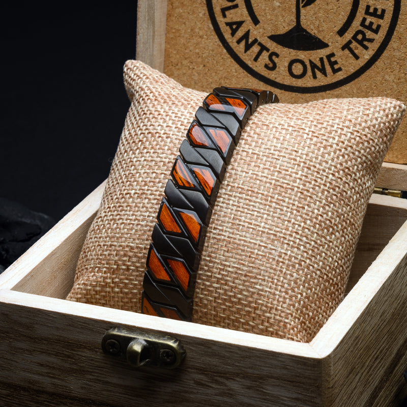 Wristband with black and Rosewood geometric pattern on a textured pillow inside a wooden box, with a brand logo in the background.