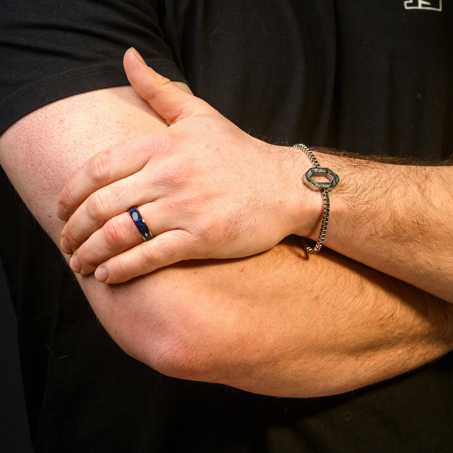 Close-up of a person's arm with a key-shaped bracelet and a blue ring.