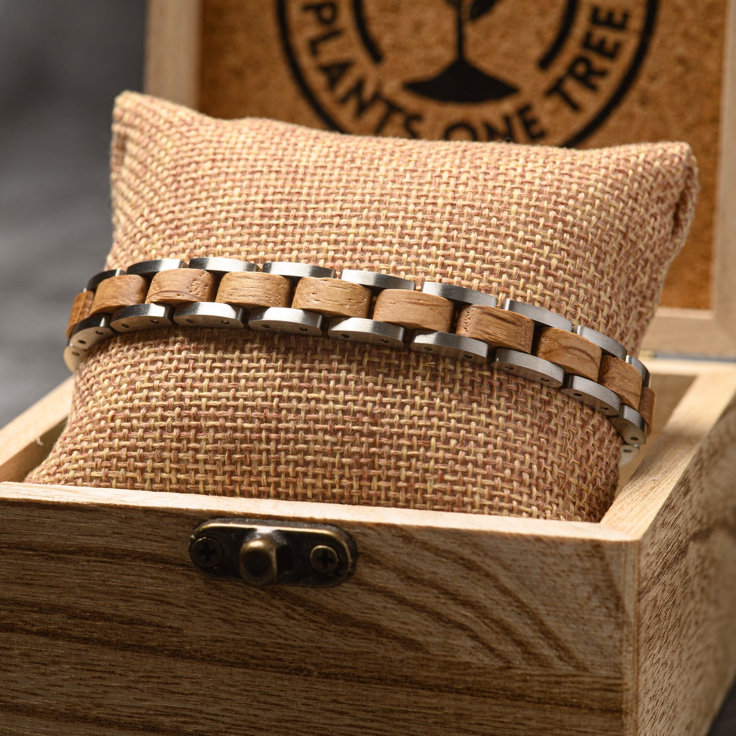 A silver steel and whiskey wood bracelet wrapped around a hessian cushion sitting in a wooden jewellery box.