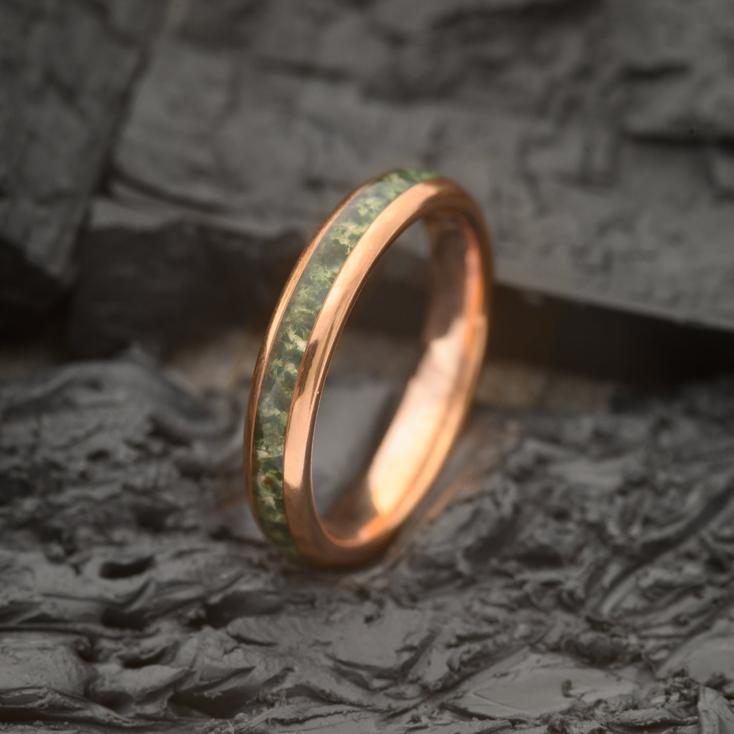 A 4mm Womens Tungsten steel ring with rosegold and moss agate sitting on a Charcoal Base