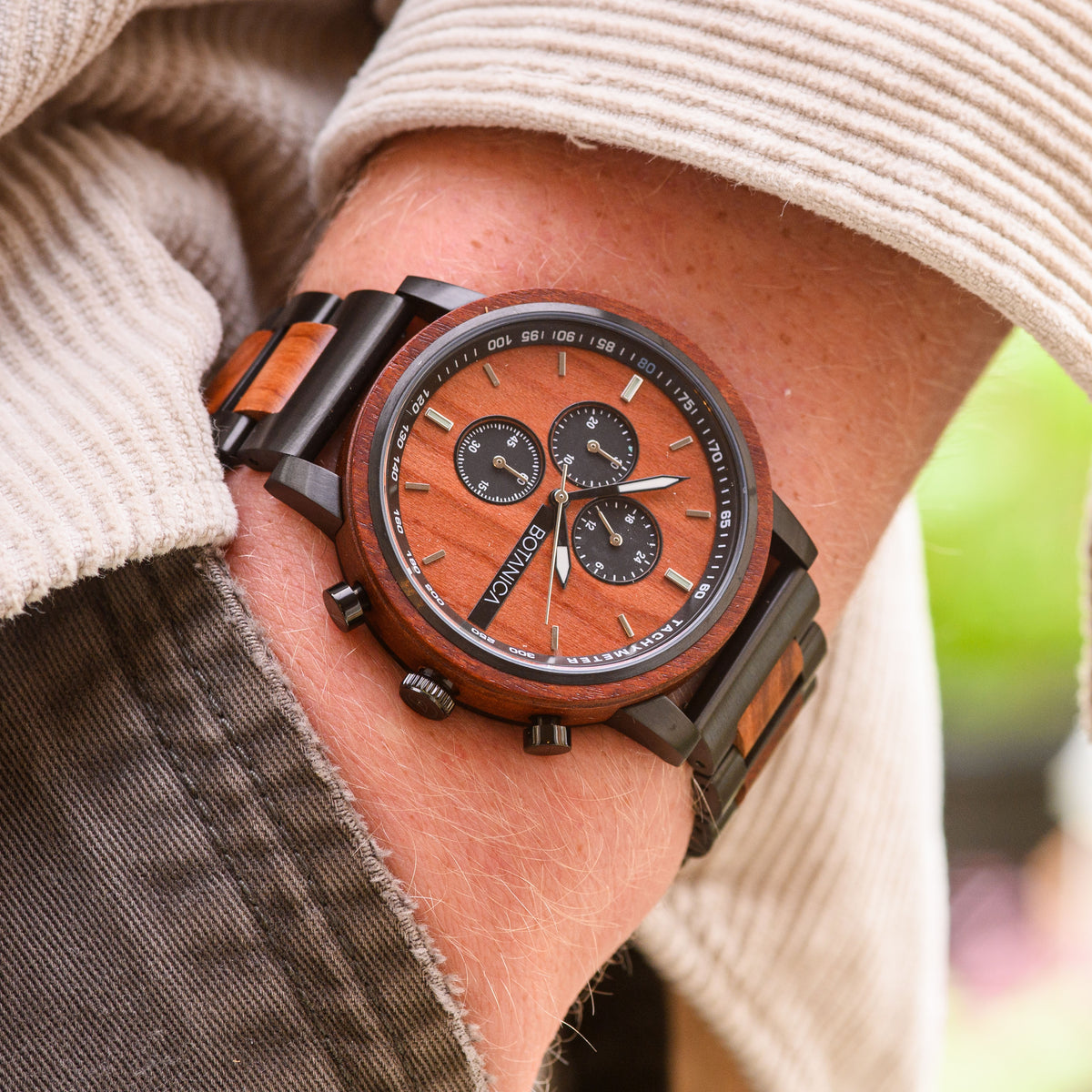 A person wearing a rosewood watch with a rosewood face and black dials.