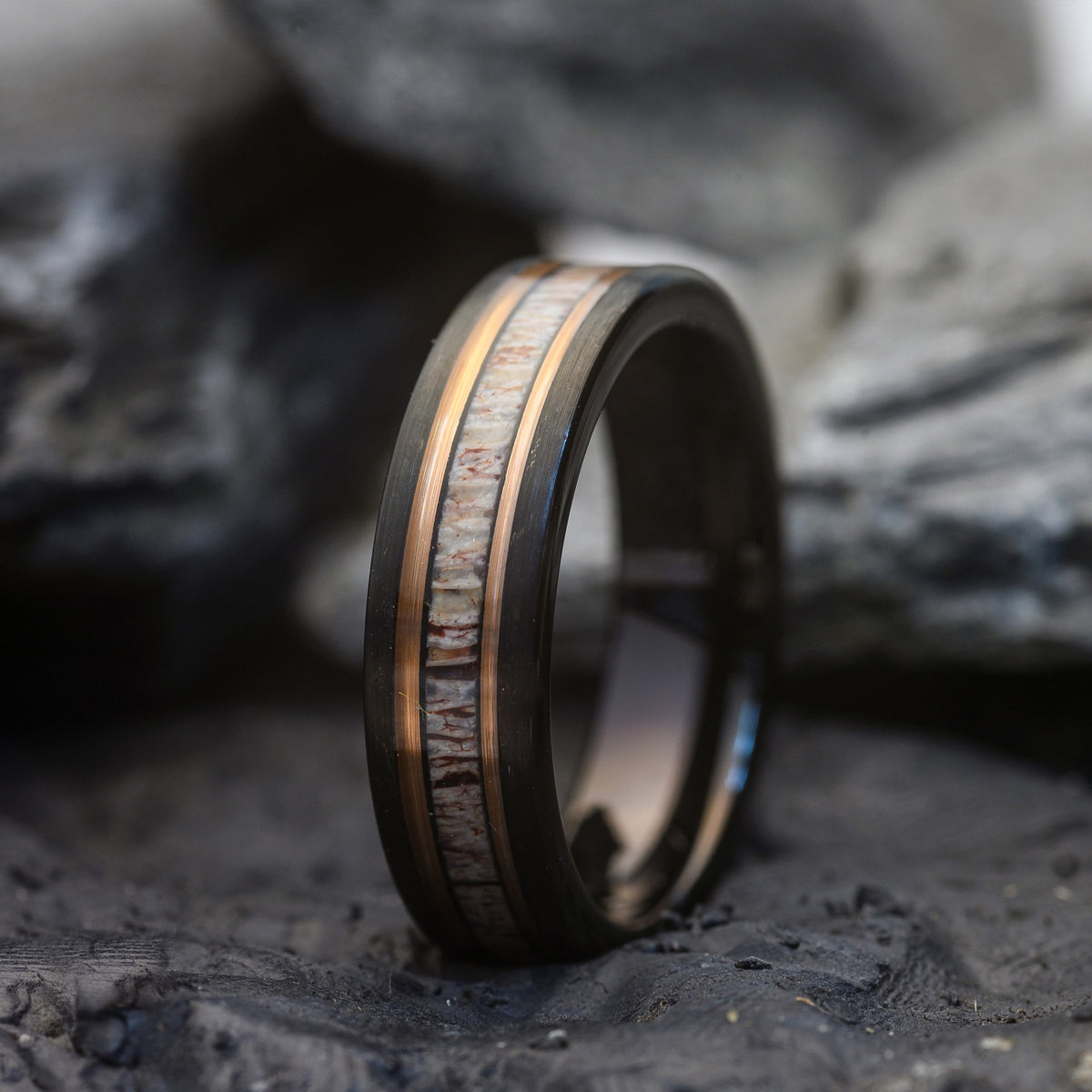 Wooden ring with Deer Antler Inlay and a Rosegold band on a dark stone surface