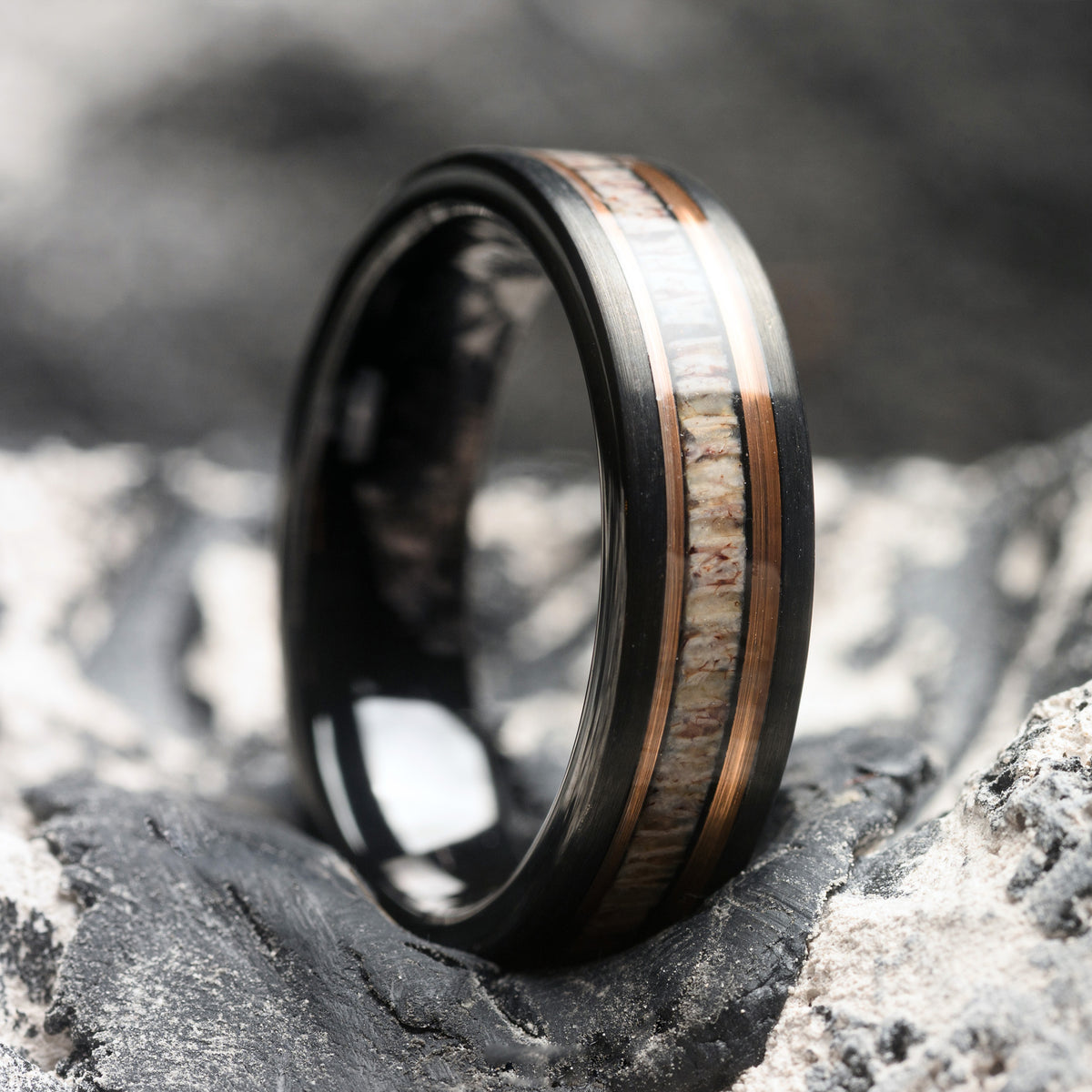 Tungsten ring with Deer Antler Inlay and a Rosegold band, on a textured stone surface