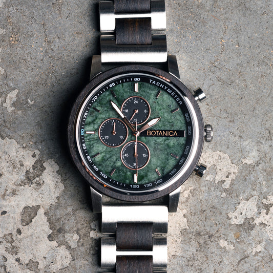 Luxury watch with green stone face and silver band on a textured surface