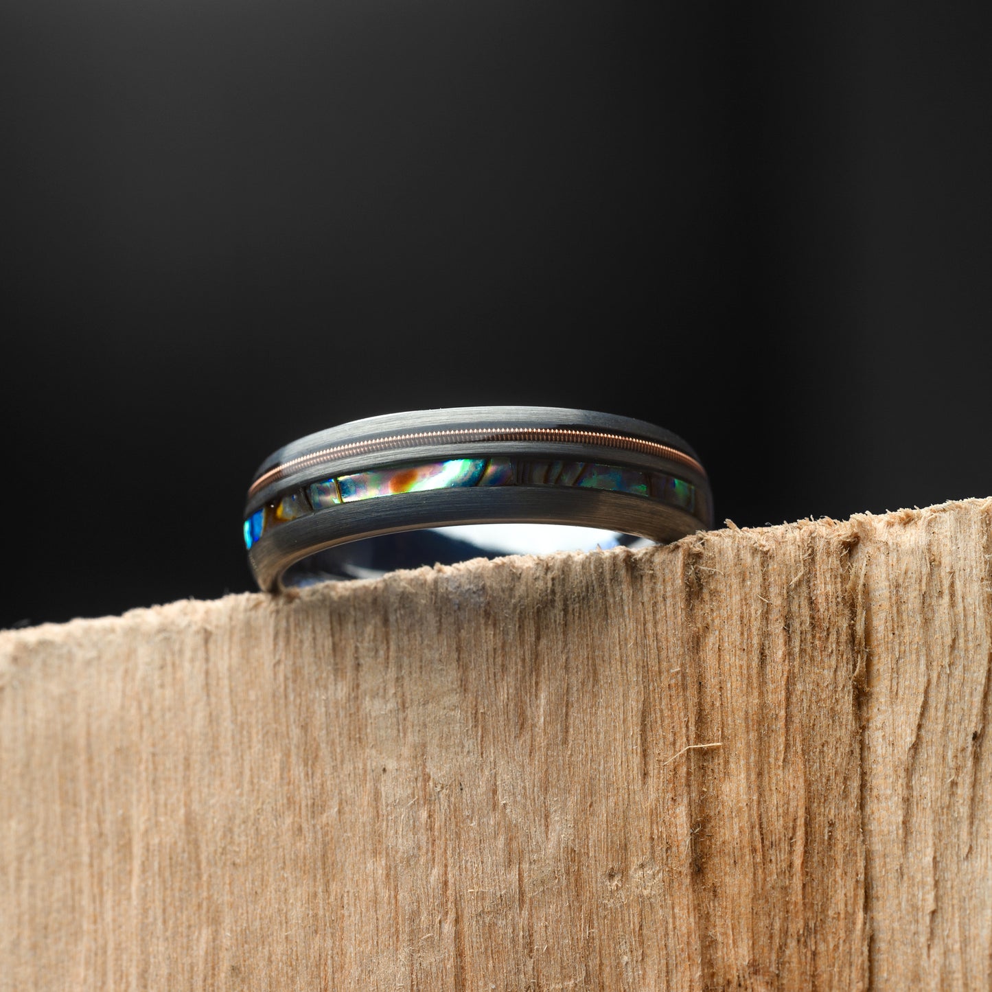 Ring with abalone shell inlay on a wooden surface against a black background