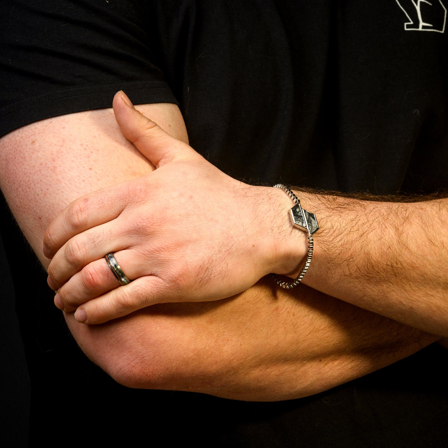 Close-up of a person's arm with a bracelet and ring on a black background