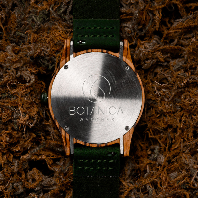 the back case of a wooden watch with a green leather strap on a mossy backdrop