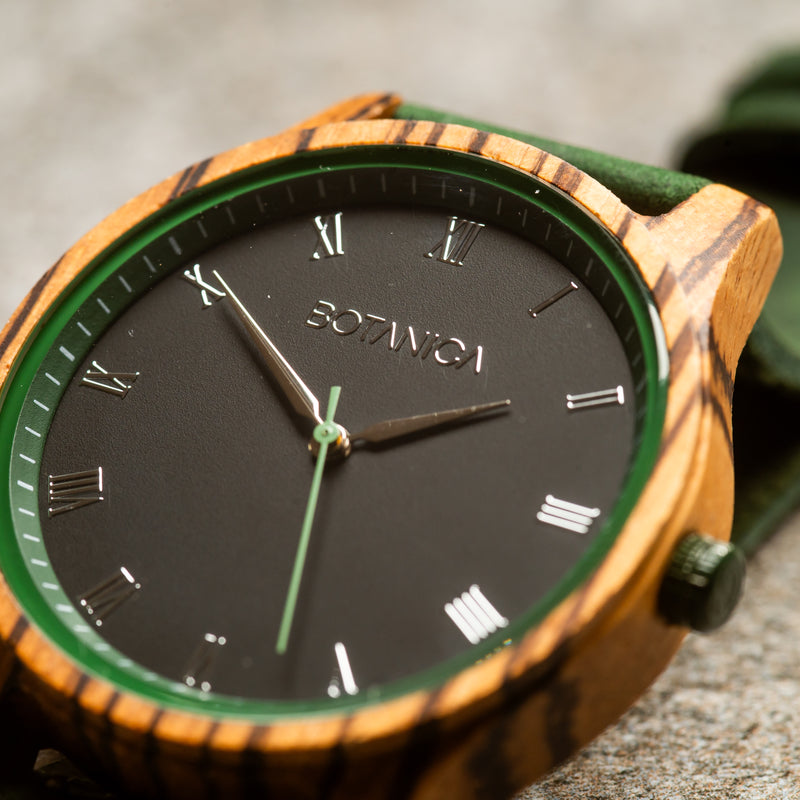 close up of a wooden watch with a roman numeral face and green leather strap
