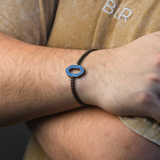 Close-up of a wrist wearing a bracelet with a blue hexagonal charm, against a blurred background.