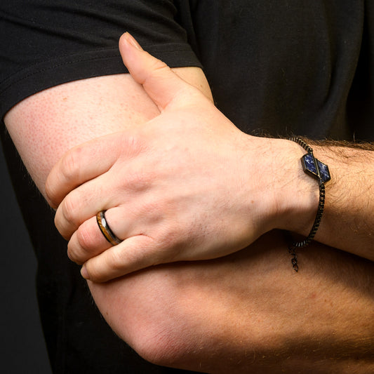 Close-up of a person's hands with a ring and bracelet on a dark background