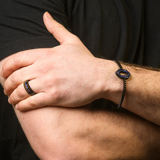 Close-up of a person's hand wearing a black bracelet and ring on a dark background