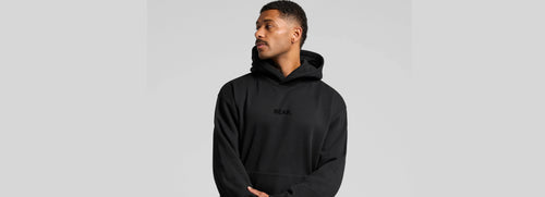Man wearing a black hoodie with a brand logo BEAR on a light gray background