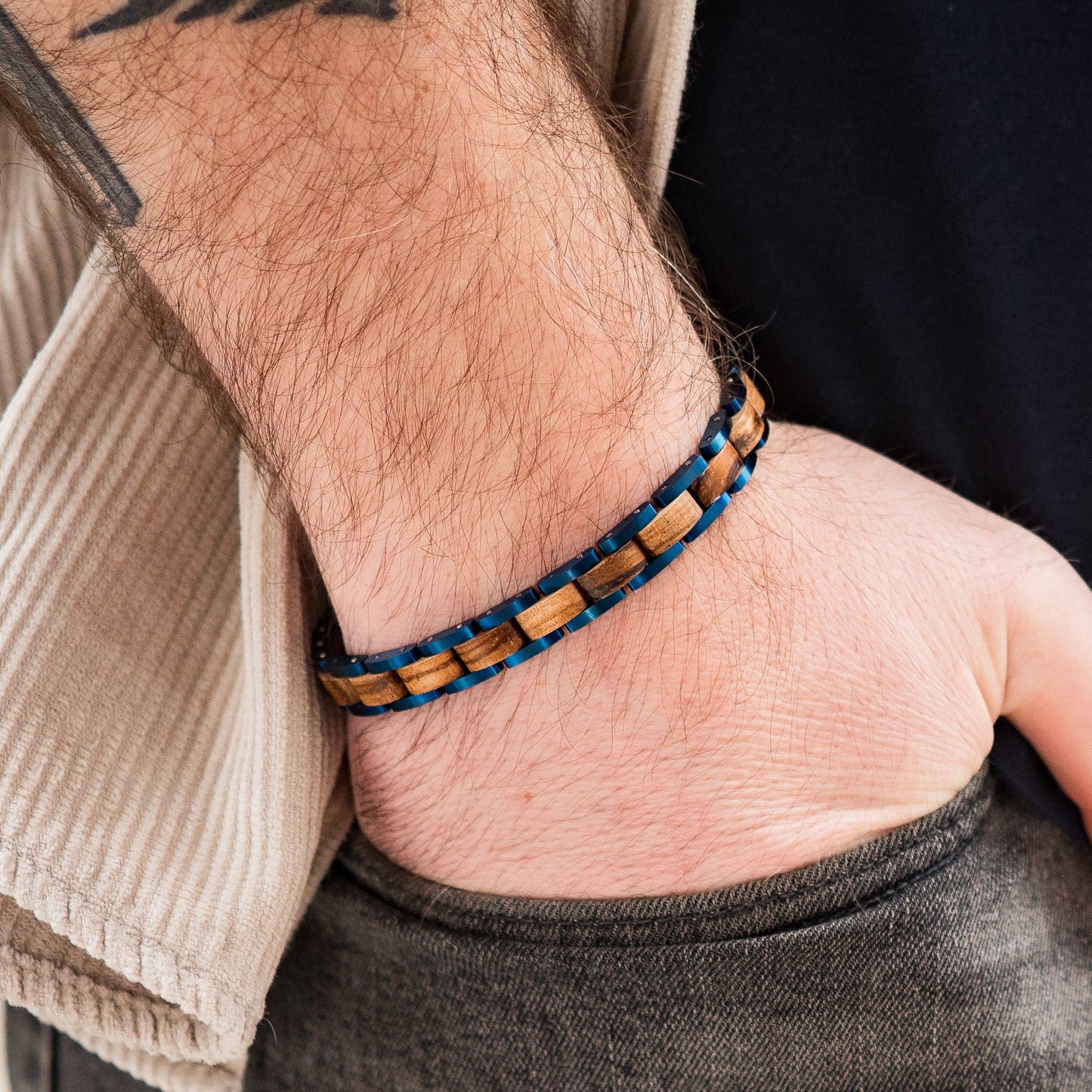 A man wearing a blue tungsten and zebrano wood link bracelet close up of hand in pocket