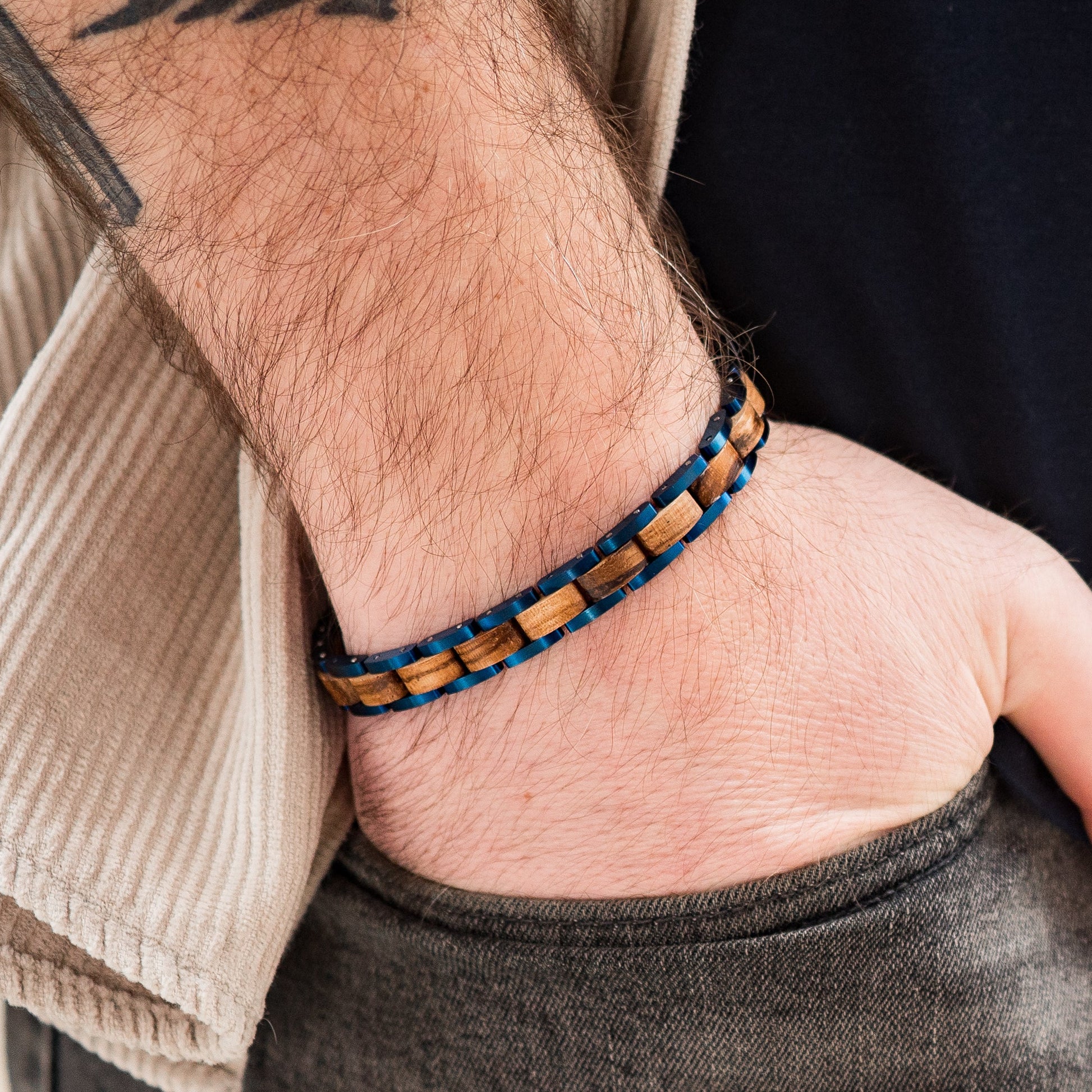 A man wearing a blue tungsten and zebrano wood link bracelet close up of hand in pocket