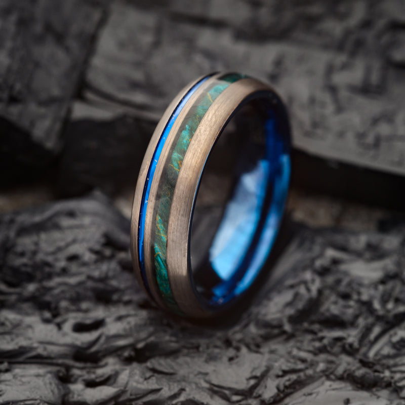 A Canadian Maplewood Tungsten Ring  with a Blue band Sitting on a Charcoal Rock