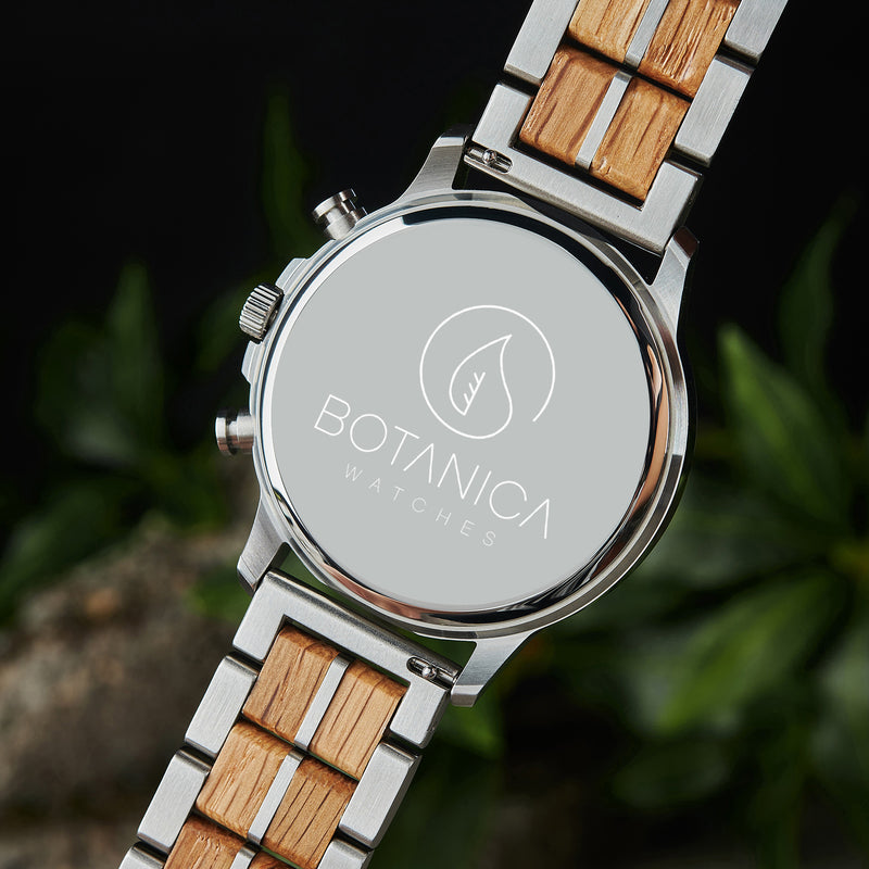 Watch with wooden and metal strap featuring Botanica Watches logo against a blurred natural background