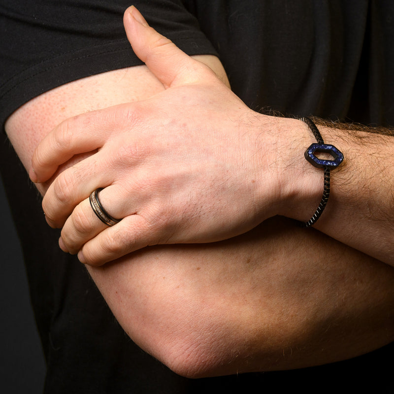 Close-up of a person's arm with a bracelet and ring on a dark background