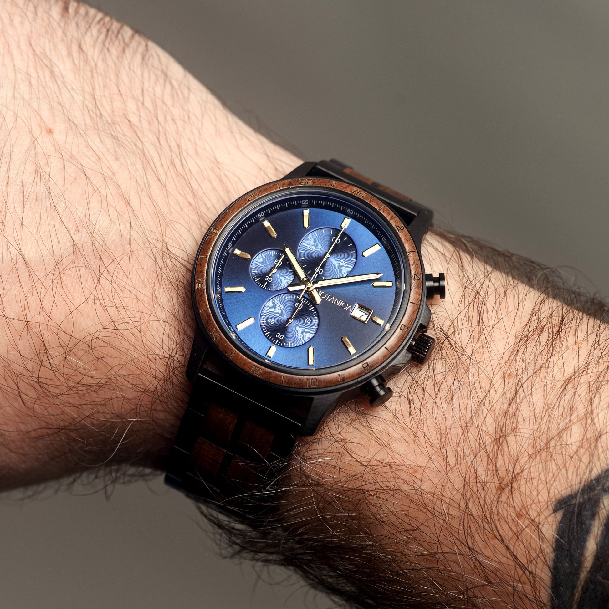 Wrist wearing a wooden watch with a blue face on a neutral background