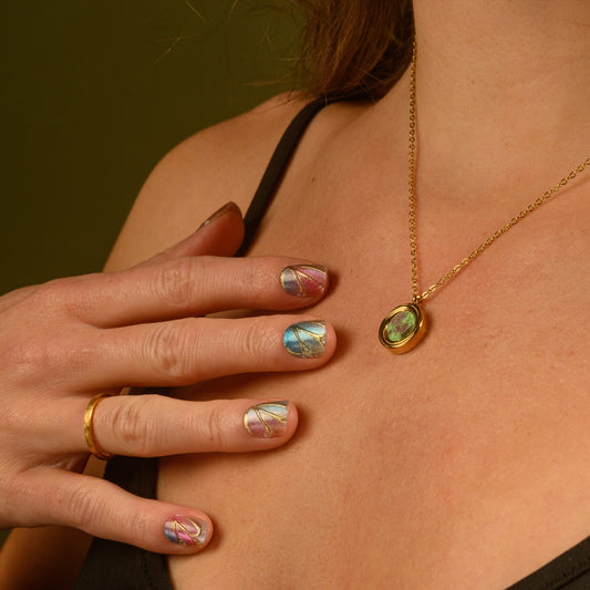 Necklace with a green gemstone worn by a person, with a hand wearing a gold ring touching the shoulder.