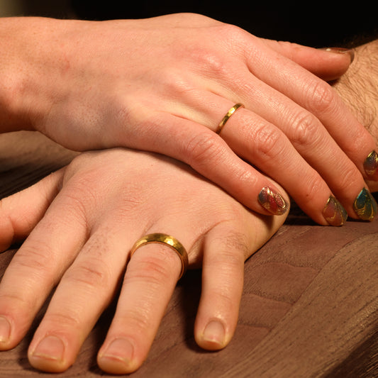 Two hands with gold rings on a wooden surface
