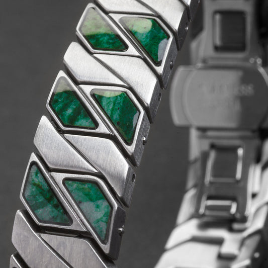 Close-up of a metallic bracelet with green gemstones on a dark background