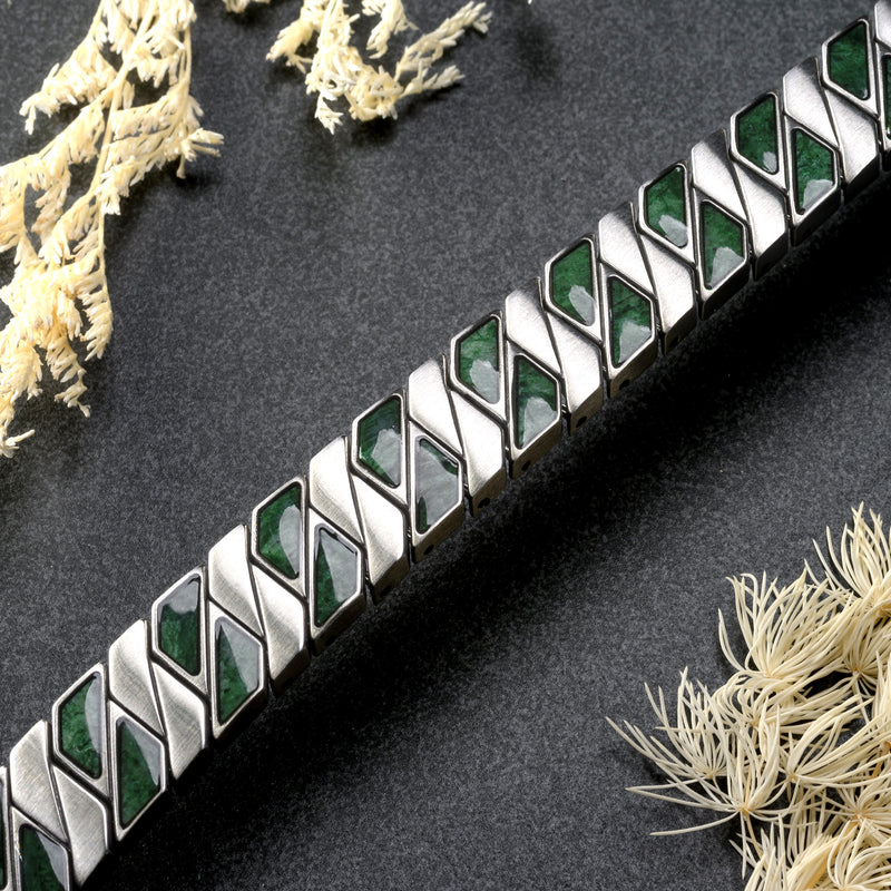 Silver bracelet with green stones on a dark surface with dried plants