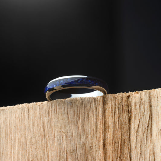 Silver ring with blue accents on a wooden surface against a black background