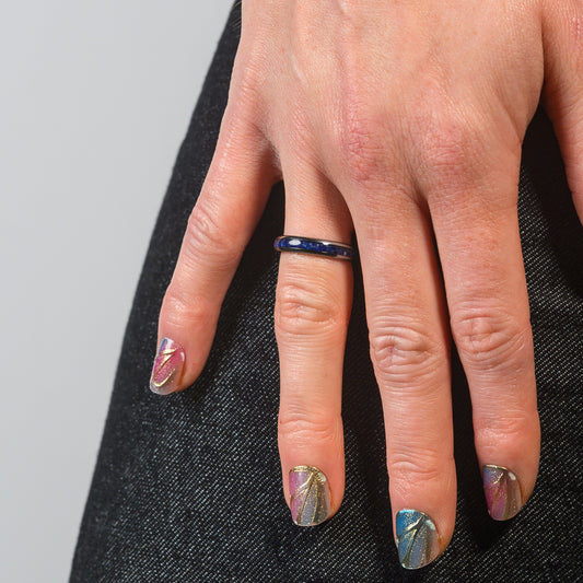 Close-up of a hand with decorative nails and a ring on a gray background