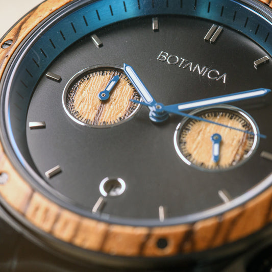 Close up detail of chronograph wooden watch highlighting the botanica logo and zebrano wood bezel and blue inner dial workings.