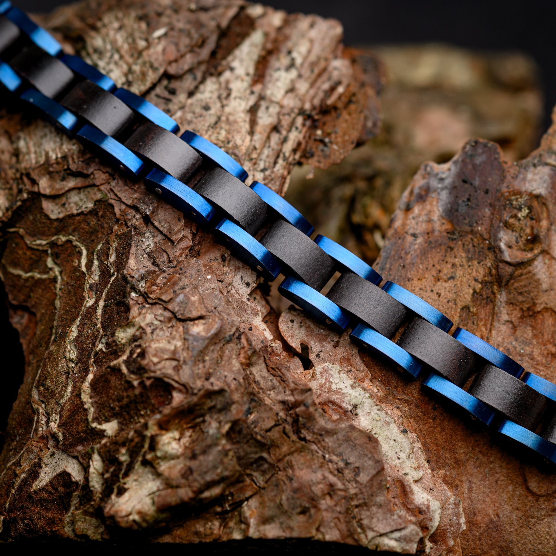 A Mens Adjustable Bracelet with Sandalwood and Blue Steel resting over a piece of drift wood