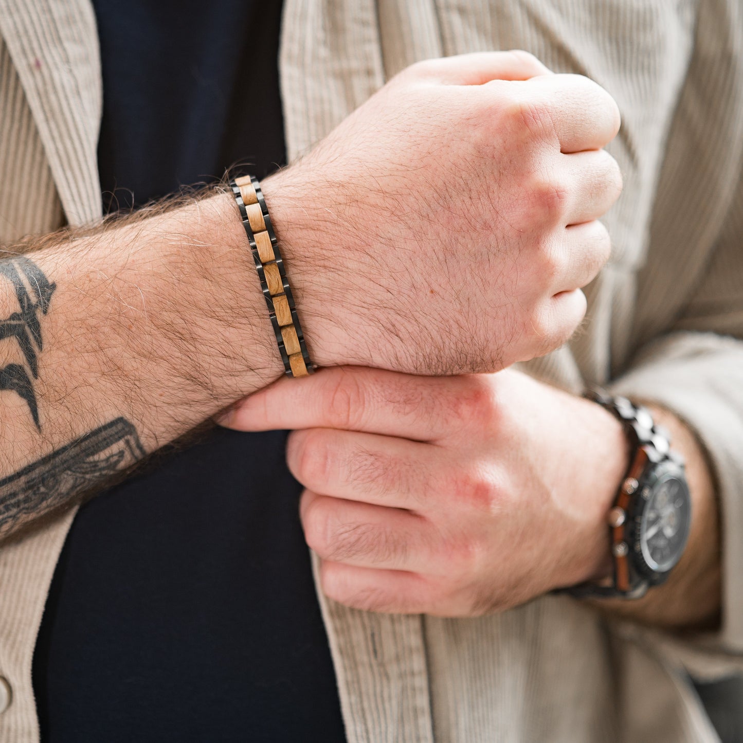 A man wearing a tungsten steel and wood bracelet holding his wrist, backdrop of other arm with wooden watch and chest area