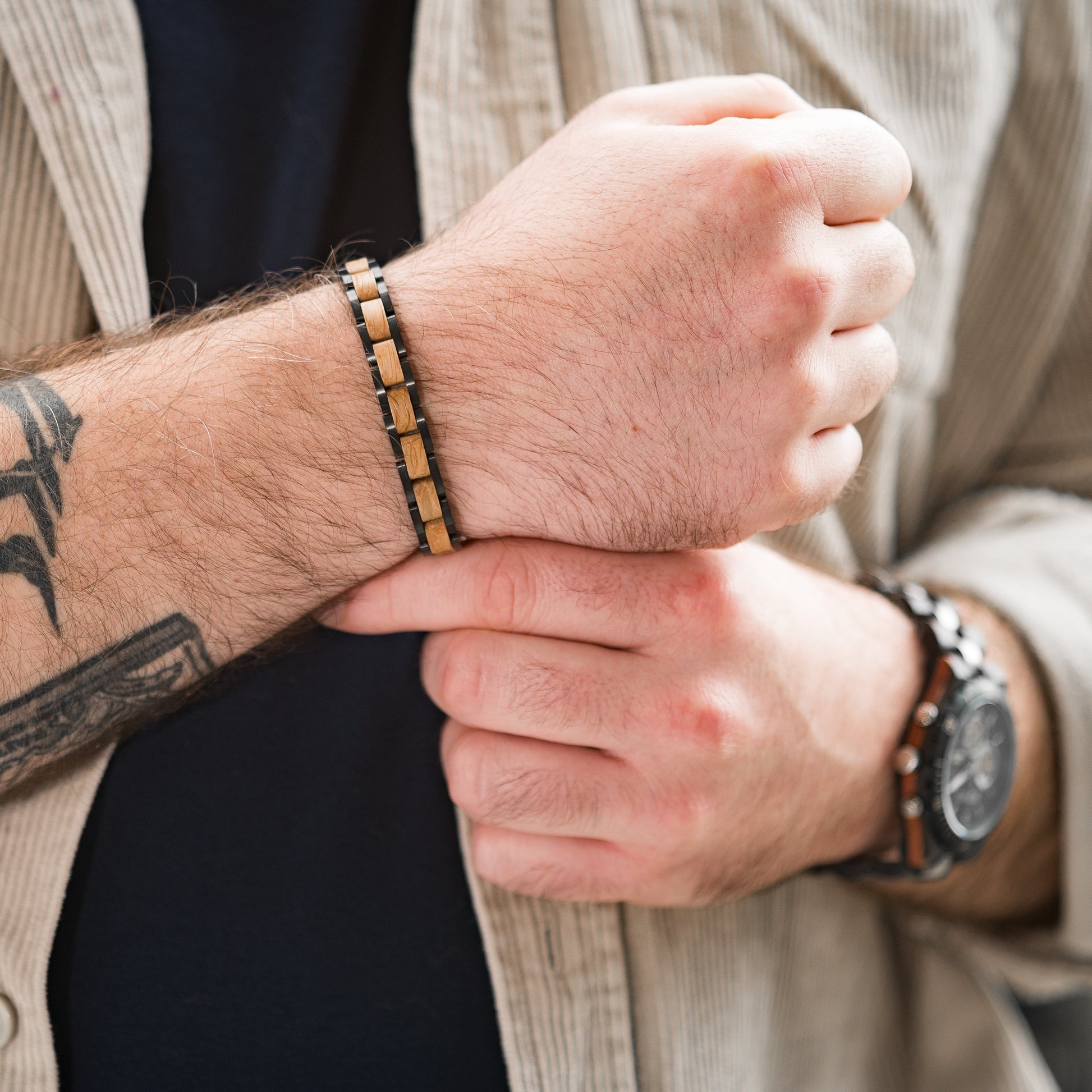 A man wearing a tungsten steel and wood bracelet holding his wrist, backdrop of other arm with wooden watch and chest area