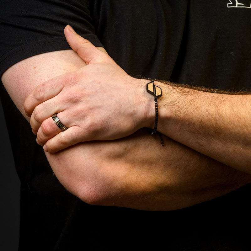 Close-up of a person's arm with a bracelet and ring, wearing a black shirt.