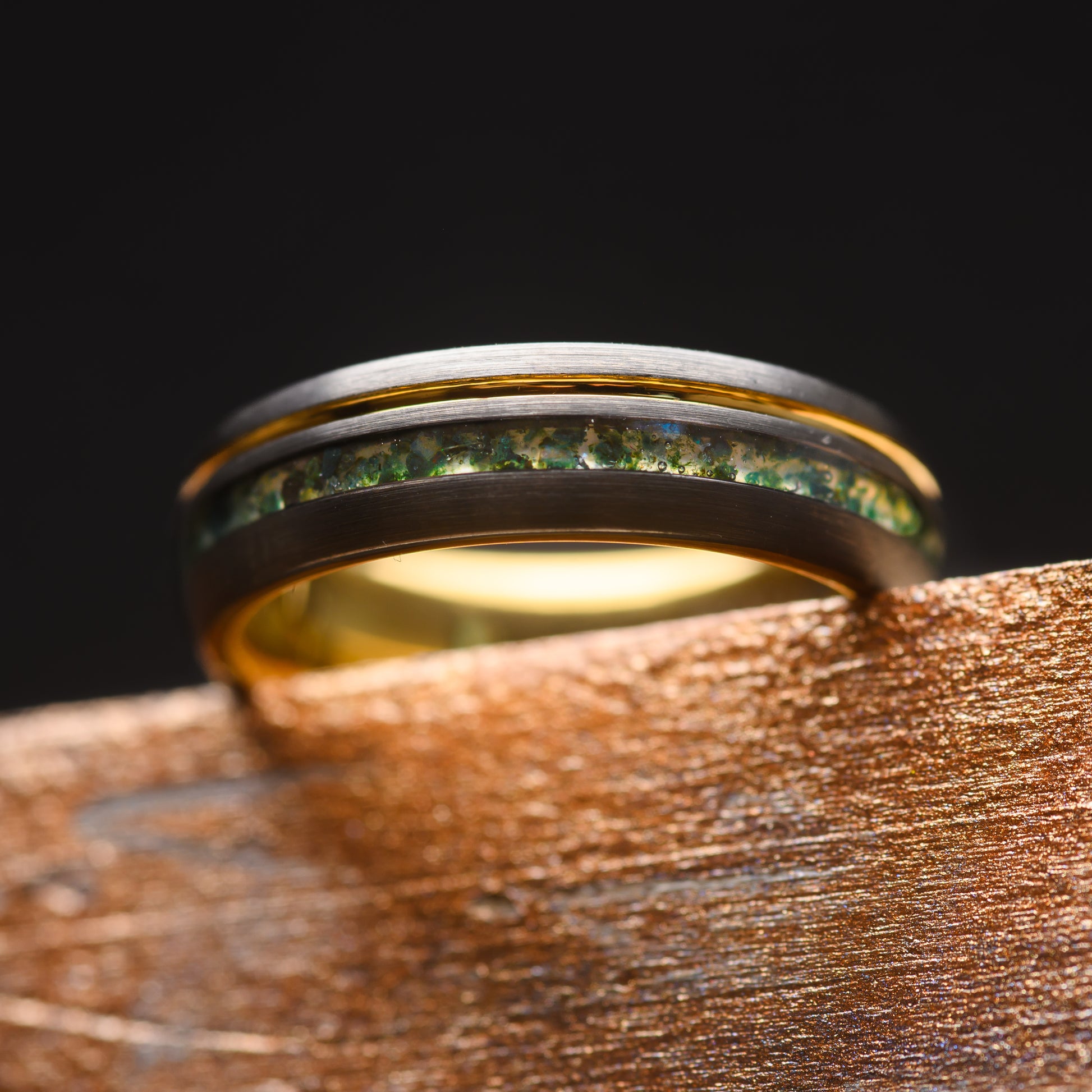 A Moss Agate and Tungsten Steel Ring balanced on a piece of wood showcasing the gold band inlay