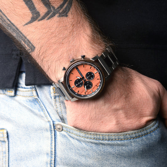 Close-up of a wrist wearing a watch with a red face and black accents, against a denim background.