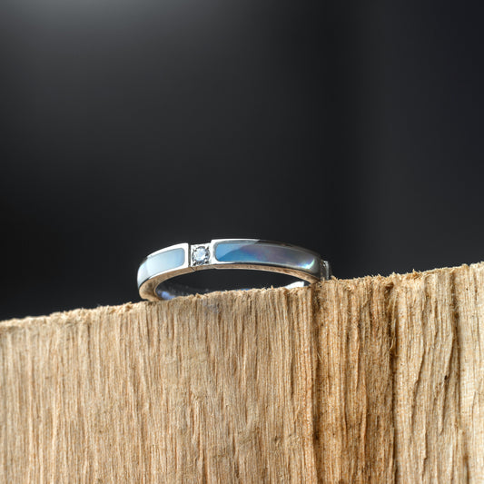 Silver ring with a diamond on a wooden block against a black background