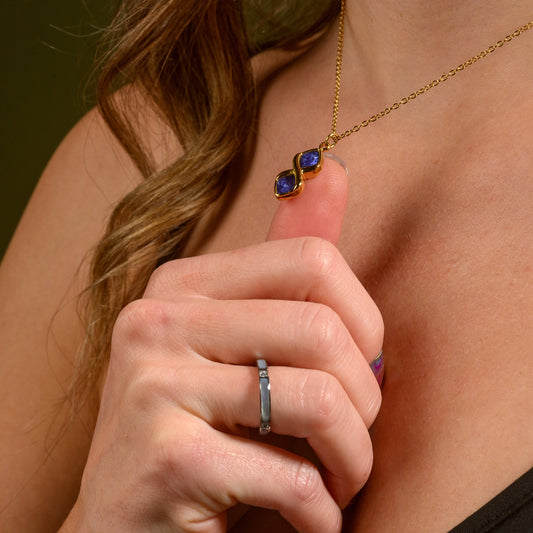Gold necklace with blue stones held by a hand against a neutral background