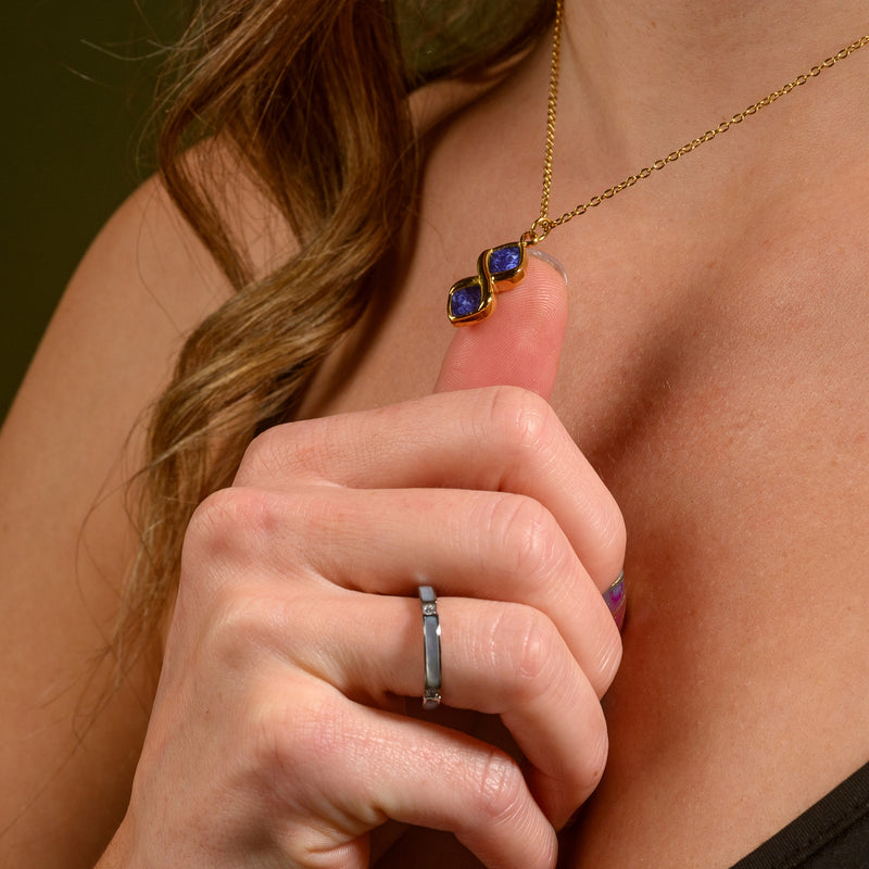 Gold necklace with blue stones held by a hand against a neutral background
