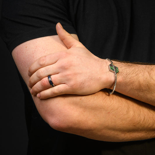 Close-up of a person's arm with a bracelet and ring on a black background