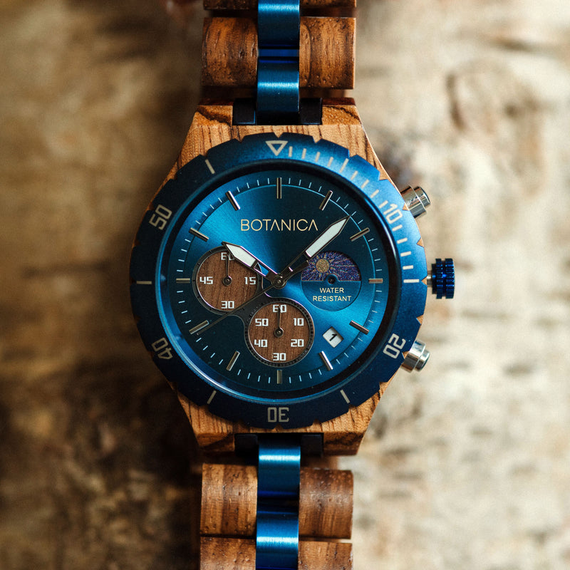 A Wooden watch with a blue dial and silver hands, featuring a wooden band and a date display, set against a textured background.