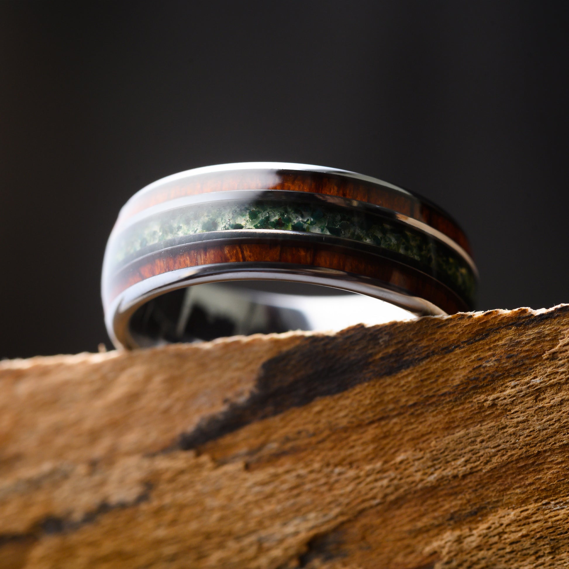 silver ring with moss agate and rosewood inlay resting on textured shelf 