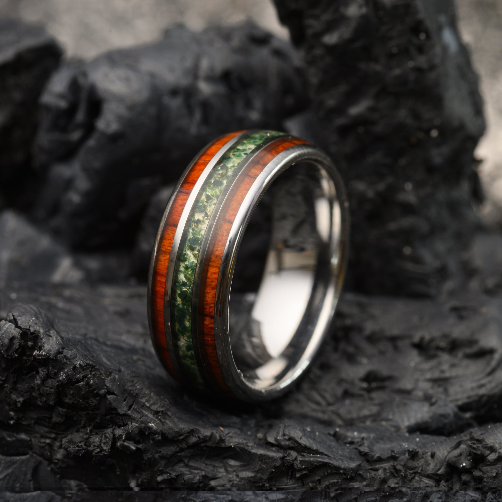Silver tungsten ring with moss agate and rosewood inlays resting on a stone background for men or women