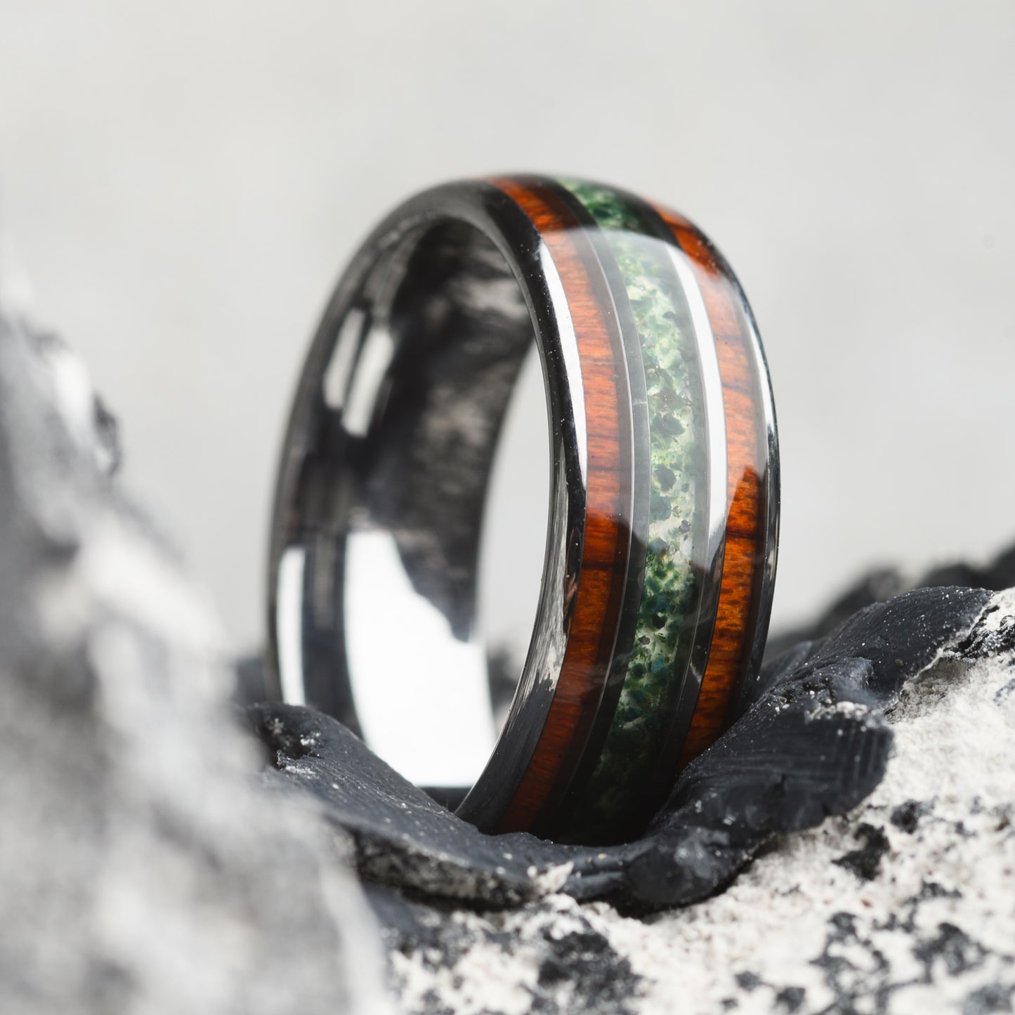 tungsten ring with stone and wood inlay resting on stone background