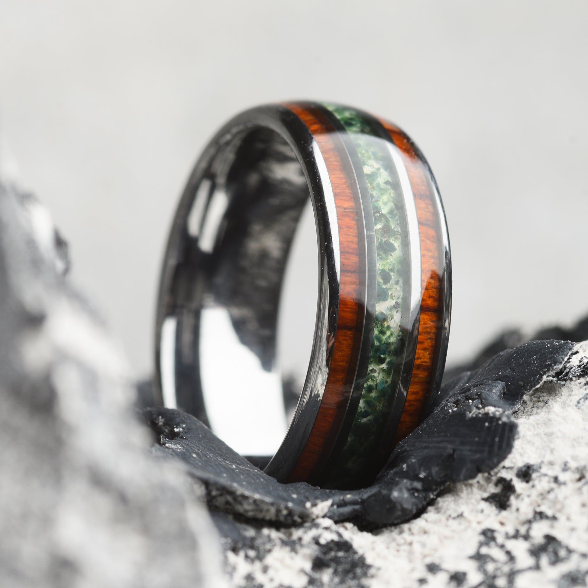 tungsten ring with stone and wood inlay resting on stone background